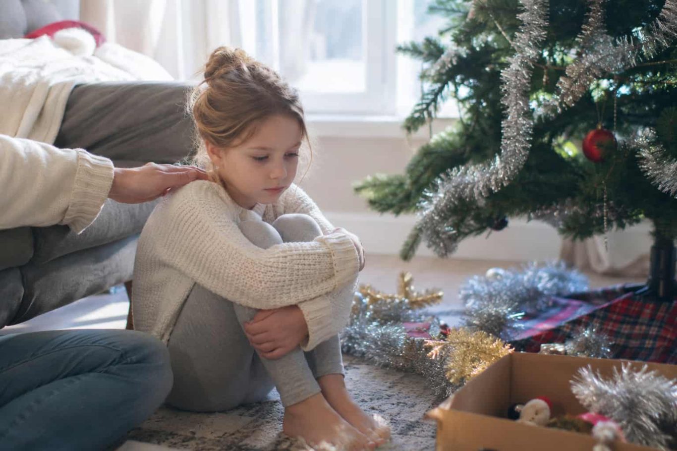 Kind sitzt allein neben Weihnachtsbaum – Kind nach Weihnachten unruhig und überfordert Kind sitzt allein neben Weihnachtsbaum – Kind nach Weihnachten unruhig und überfordert
