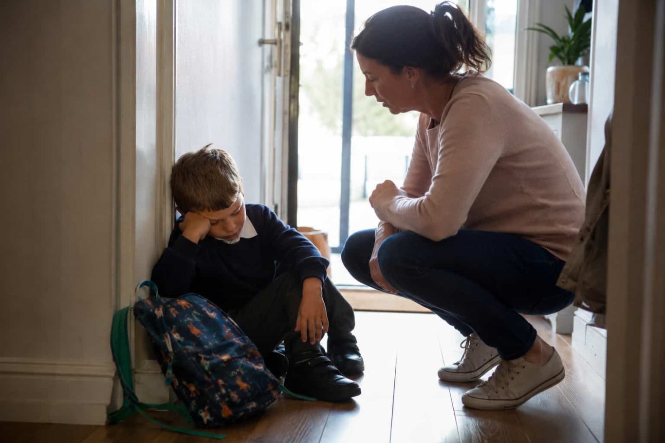 Erwachsener kauert neben Kind mit Schulrucksack – Kind nach der Schule gereizt Erwachsener kauert neben Kind mit Schulrucksack – Kind nach der Schule gereizt