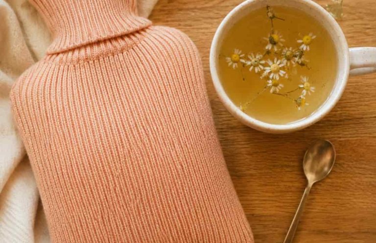 koerperfluestern-hausmittel-bauchweh-kind-waermflasche-tee Wärmflasche und Kräutertee auf Holztisch — einfache Hausmittel bei Bauchweh bei Kindern